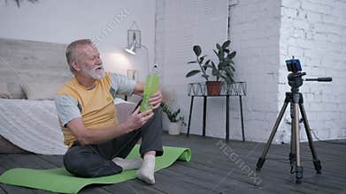 Old blogger, aging man influencers love sports takes a drink review on smartphone for vlog recommending water to