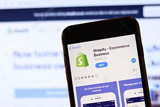 Phone with Shopify icon on screen close up with blur website on laptop. Los Angeles, California, USA - 30 November 2019,