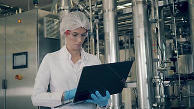 Quality control of production line at a factory. Woman works with laptop while checking dairy plant machines.