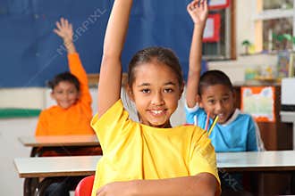 Three primary school children hands raised in clas
