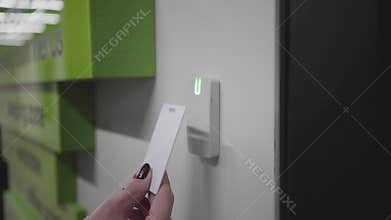Close-up of closed electronic lock in open space office. Female Caucasian hand holding key card in front of lock, light