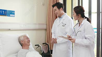 Asian doctors talking to senior patient in hospital ward