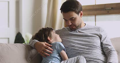 Caring dad embracing preschool son having trust conversation on sofa