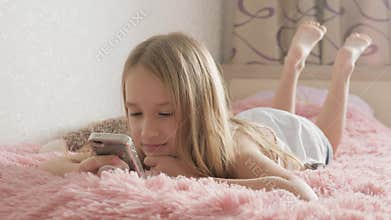 Curious girl using phone apps looking at cellphone device sitting on bed, child and gadget concept.