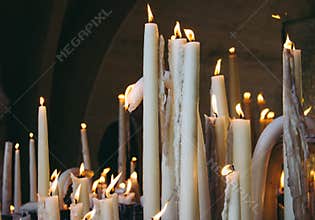 Big burning candles from prayers for hope. Saint Bernadette grotto with many white candles with flame. Sanctuary in Lourdes.