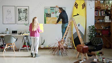 Creative couple hangs painting in modern apartment