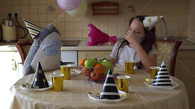 A girl in a festive cap and a medical mask sits at the table alone on her birthday. Depression from lack of friends. Coronavirus