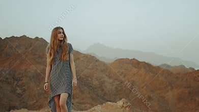 Young blond woman in long dress walks on top of mountain. Mountain landscape with sunset, slow motion, full hd