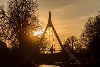 Silhouette of woman on bicycle on suspended bridge under the river by sunset