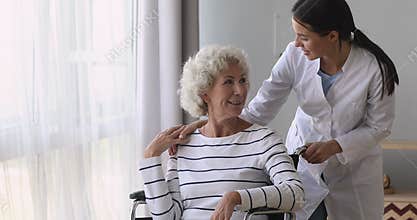Pleasant young caregiver volunteer medical worker talking to disabled woman.