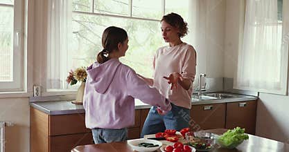 Mom and daughter enjoying funny dance in kitchen cooking together