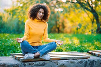 Young beautiful african american woman meditating at city park, she feeling peace in megalopolis. Zen, freedom, calmness