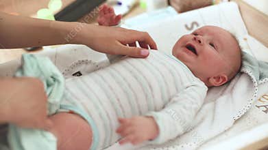 Mother playing with her infant baby son on the changing table, going over his belly with fingers