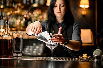 Bartender pouring ice cubes into glass on bar counter.