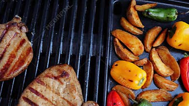 Grilled cooking pork loin chops and potatoes wedges on grill, barbecue, hot cast iron. close up