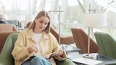 Smart girl student holding book sitting in university library campus.