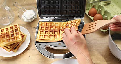 Women's hands take out cooked waffles from electric waffle iron.