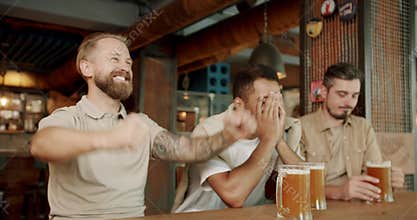 Young men drink beer and watching sport game at pub