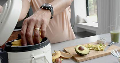 Midsection of senior biracial man preparing smoothie, composting bio waste in kitchen, slow motion