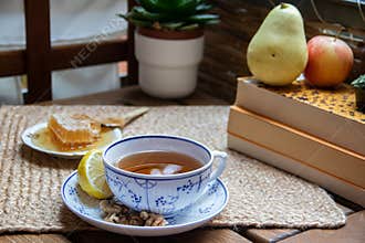 Morning setup on wooden table at balcony for morning relaxation with books, cup of tea, teapot, organic honey, green tea leaves