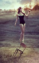 Beautiful girl balances on back of chair outdoors.