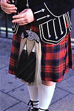 Scottish man wearing kilts playing the bagpipes.