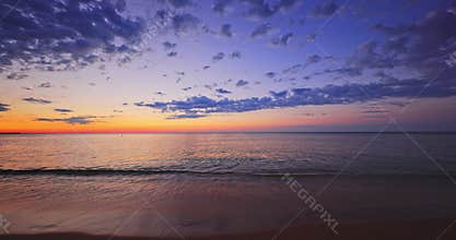 Sunrise over sea sand and lonely island beach. Burning sun is rising up over ocean waves.