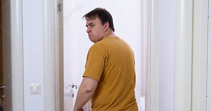 Childish young man walks down corridor, stops in doorway, turns around to make an offended grimace, and then enters the