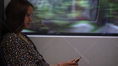 Close shot of young attractive Ukraine female in glasses sitting on moving city metro train. Woman calling typing text