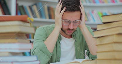 A tired student sits at desk full of books. Young man preparing for an exam in the college library. Self education
