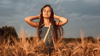 Portrait of Little girl with long brown hair, walk in a wheat field on a summer evening