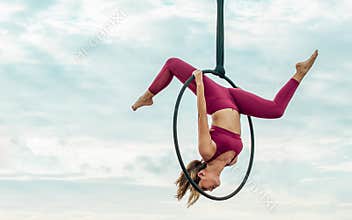 Beautiful healthy strong woman wearing sport bra, relaxing, exercise yoga fly in air, aerial hoop on outdoor rooftop in morning.
