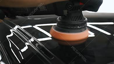 Close-up of the moment when mechanic is polishing black car and using polishing machine. Focus on machine operation.