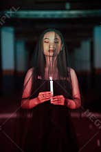 a female devil worshiper with a transparent veil is performing a spooky ritual by holding a candle in her hand