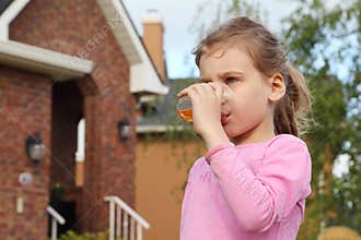 Girl stands near cottage and drinks juice