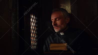 Pastor listening to someone's confession in confessional booth and nodding with understanding. Catholic priest