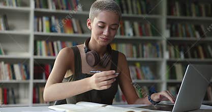 Teen girl studying in library, doing assignment using computer