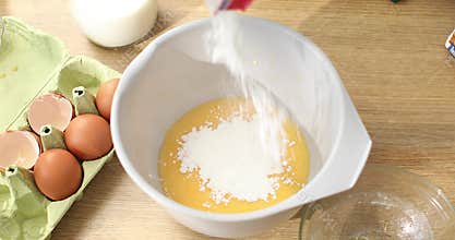 Flour is added to a bowl with beaten eggs.