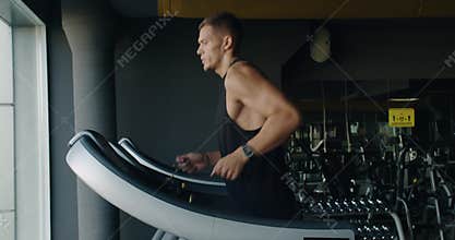 Young man with athletic body running on treadmill at gym