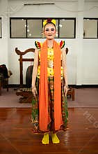 a traditional Indonesian dancer standing in a yellow costume and an orange scarf hanging down her body