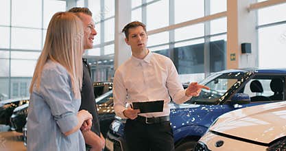 Car Dealership. Cheerful Elegant Manager Guy Showing Automobile To Customers