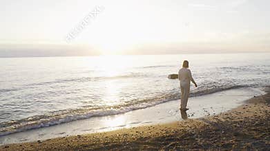 A woman walks along the seashore barefoot, enjoying the sunset.