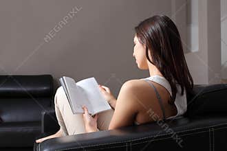 Beautiful woman at home sitting on a couch reading a book