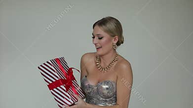 Elegant, charming, trendy blond woman in silver dress catching striped present box with ribbon from air, try to unpack