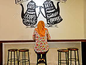 a hijab woman wearing a floral pattern shirt is visiting a cafe