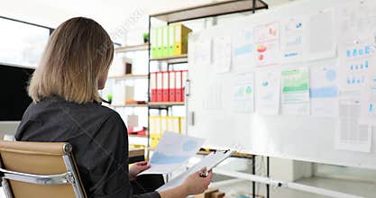 Aspiring female manager doing paperwork doing research using statistical information on white board in office