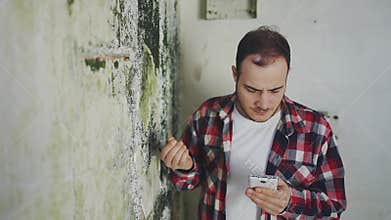 portrait man in a shirt with a phone in his hands examines a wall with mold ,searching the Internet for a disinfection