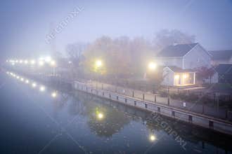 Two story house with American flag in mist foggy early morning along historic Erie Canal with yellow pole lighting, colorful fall