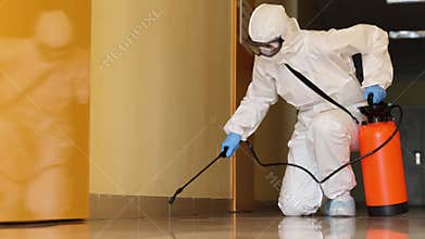 Worker in hazmat suit diligently sprays disinfectant on floor