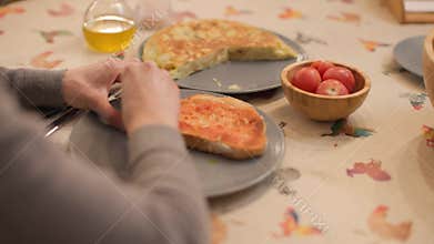 Hands rubbing tomato on toast with Spanish omelet and olive oil in background